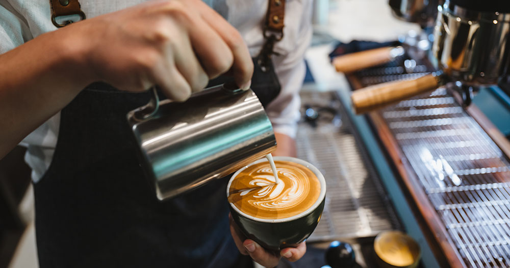 barista making latte art, shot focus in cup of milk and coffee